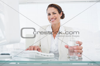 Businesswoman using computer while holding a glass of water