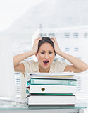 Angry businesswoman shouting with stack of folders at desk