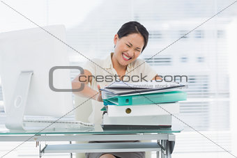 Angry businesswoman with stack of folders at desk