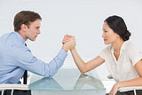 Business couple arm wrestling at desk