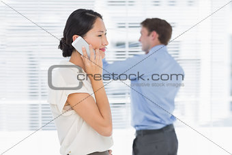 Businesswoman using cellphone with man behind at office