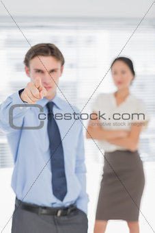 Businessman pointing towards camera with woman in office