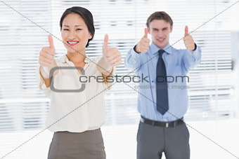 Business colleagues gesturing thumbs up in office
