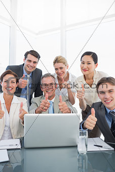 Business colleagues with laptop gesturing thumbs up at desk
