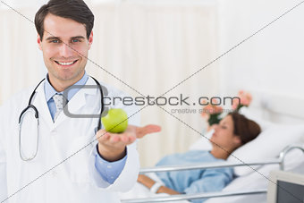 Smiling doctor holding apple with patient in hospital