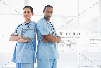 Confident surgeons standing back to back in hospital