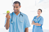 Male surgeon holding an apple with colleague behind
