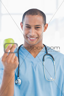 Portrait of a smiling surgeon holding an apple