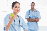 Smiling surgeon holding an apple with colleague in hospital