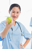 Smiling female surgeon holding out an apple in hospital