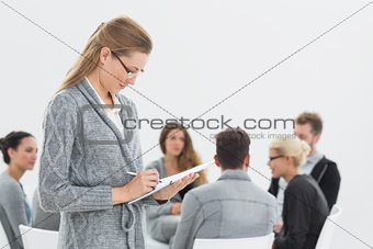 Therapist writing notes with group therapy in session