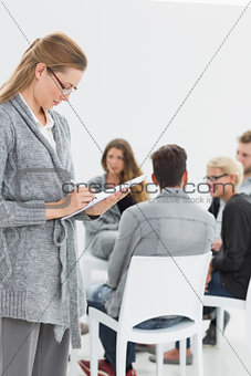 Therapist writing notes with group therapy in session