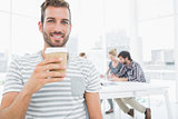 Man holding disposable coffee cup with colleagues in background
