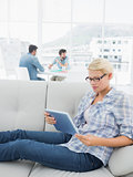 Woman using digital tablet with colleagues in background at creative office