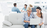 Women using laptop with colleagues in background at creative office