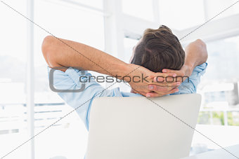 Rear view of a casual man resting with hands behind head in office
