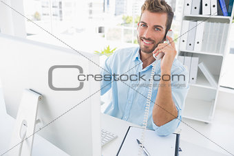 Smiling man using phone and computer in office