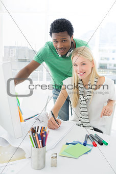 Artist drawing something on paper while using computer with colleague