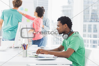 Casual man using computer with group of colleagues behind in office