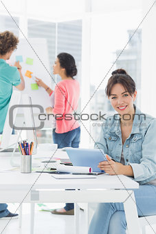 Casual woman using digital tablet with colleagues behind in office