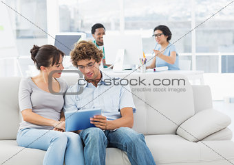Casual couple using digital tablet with colleagues at creative office