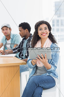 Smiling woman using digital tablet with colleagues behind in office
