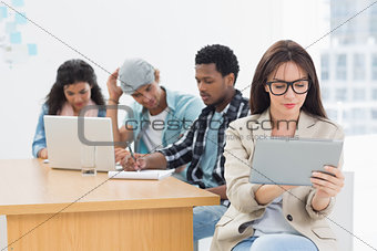 Concentrated woman using digital tablet with colleagues behind in office