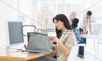 Casual woman working at desk with colleagues behind in office