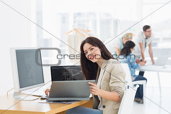 Casual woman working at desk with colleagues behind in office