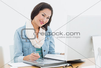 Smiling casual woman with catalog in front of computer in office
