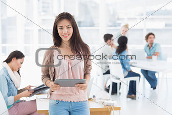 Artist holding digital tablet with colleagues in background at office