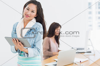 Casual female artist using digital tablet with colleague in background at office