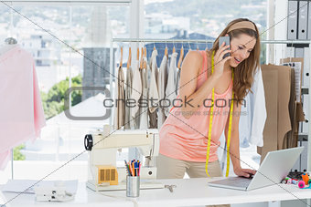 Fashion designer using laptop and cellphone in studio