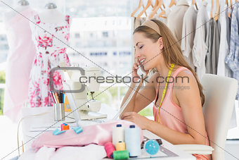 Young female fashion designer using phone in studio
