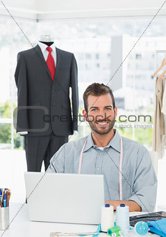 Smiling male fashion designer using laptop in the studio