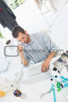 Male fashion designer using laptop and phone in studio