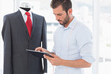 Concentrated fashion designer looking at digital tablet by suit on dummy