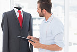 Concentrated fashion designer with digital tablet looking at suit on dummy