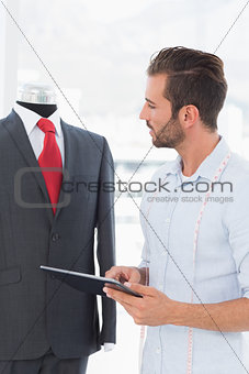 Fashion designer with digital tablet looking at suit on dummy