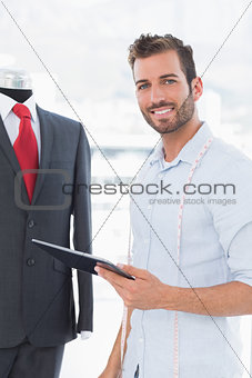 Fashion designer with digital tablet by suit on dummy