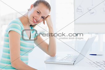 Smiling young casual woman in front of laptop at office