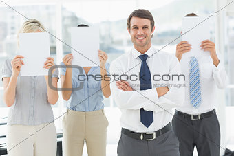 Businessman with colleagues holding blank paper in front of faces