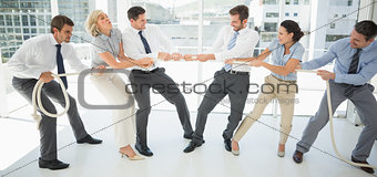Business people playing tug of war in office