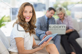 Businesswoman using digital tablet with colleagues using laptop