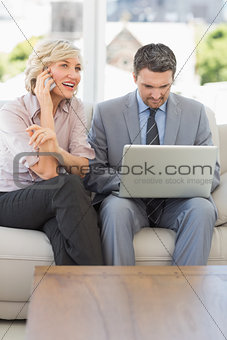 Businesswoman on call while colleague using laptop at home