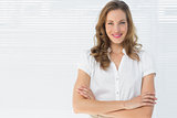 Smiling businesswoman with arms crossed against blinds