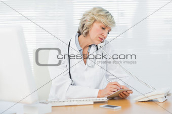 Female doctor using phone by computer at medical office