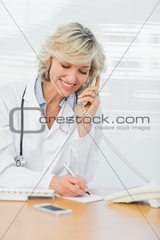 Doctor using phone while writing notes at medical office