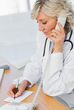 Female doctor using phone while writing notes