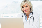 Smiling female doctor using laptop in medical office